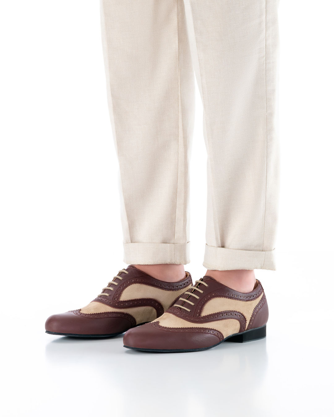 Le mannequin se tient debout, les pieds parallèles, vêtu d'un pantalon clair, en diagonale par rapport à l'appareil photo ; il porte d'élégantes chaussures de danse en cuir beige et bordeaux, ornées d'un motif brogue ajouré et dotées de lacets clairs.