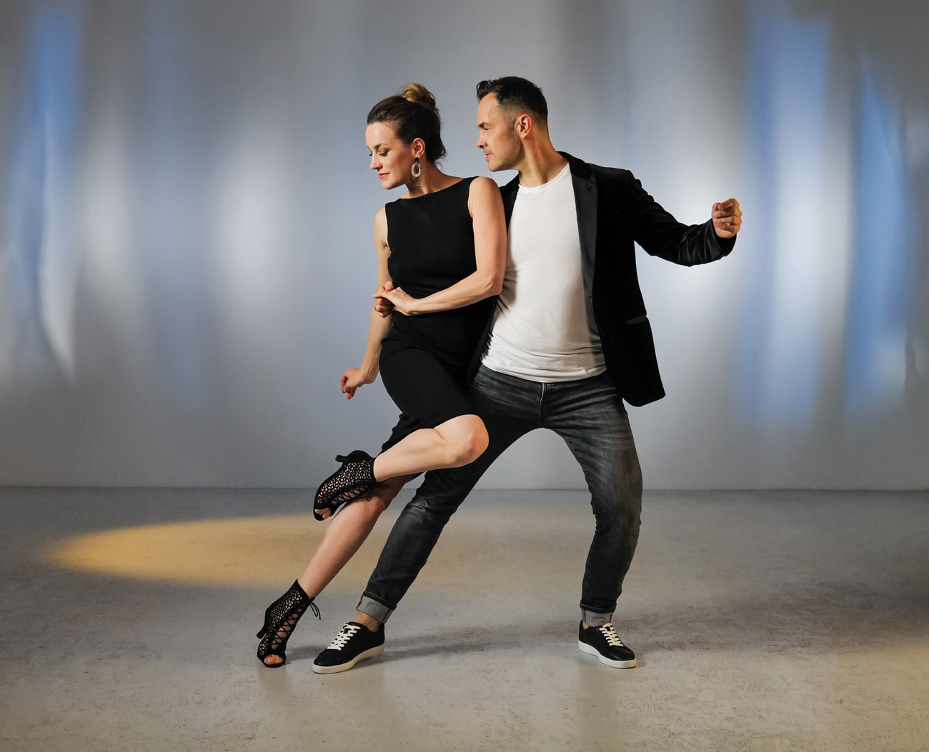 Jeune couple de danseurs prenant la pose de la salsa avec des bottines et des baskets de danse noires par Anna Kern