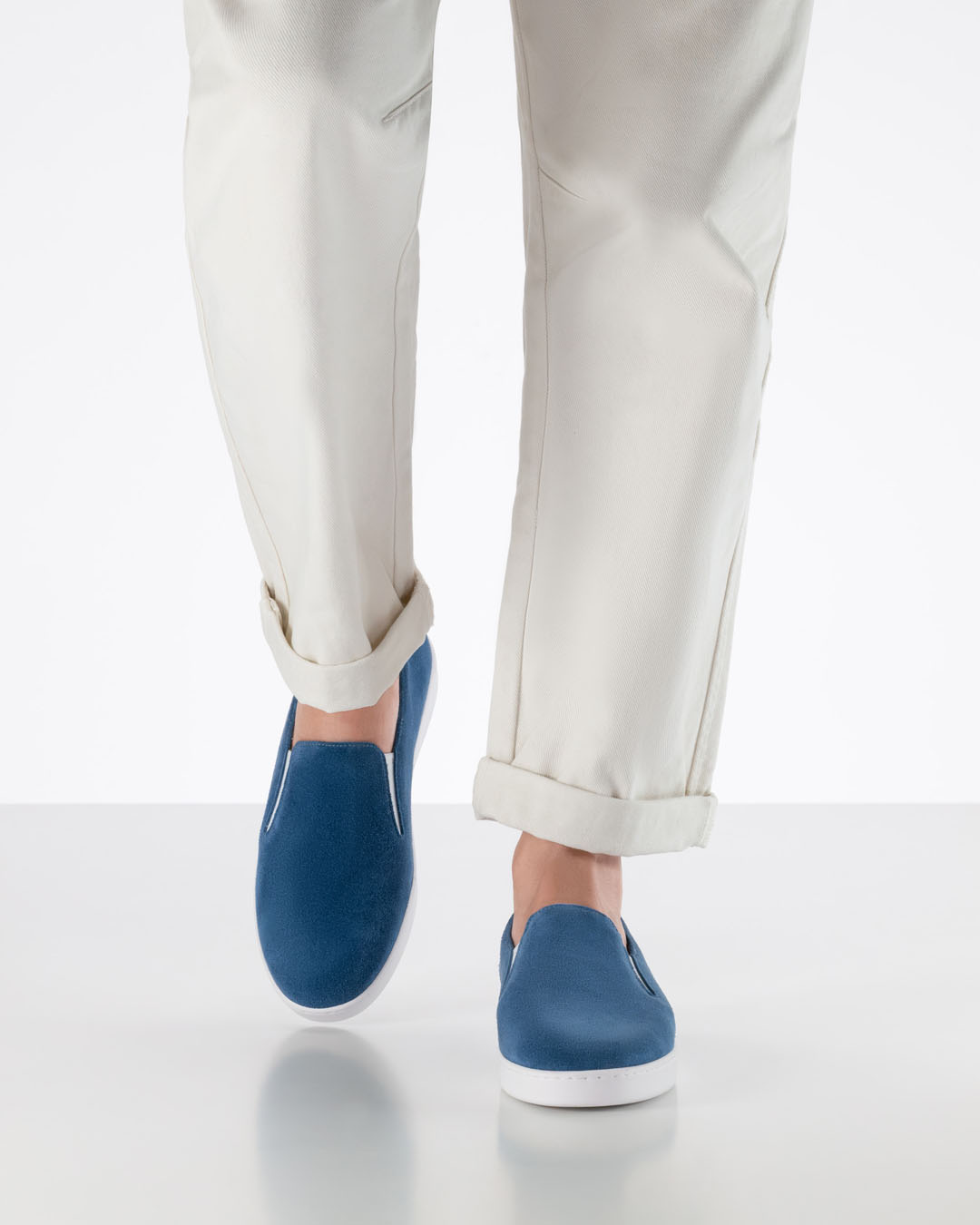 Le mannequin s'avance vers la caméra, vêtu d'un pantalon blanc et de baskets de danse bleues en daim à semelle blanche