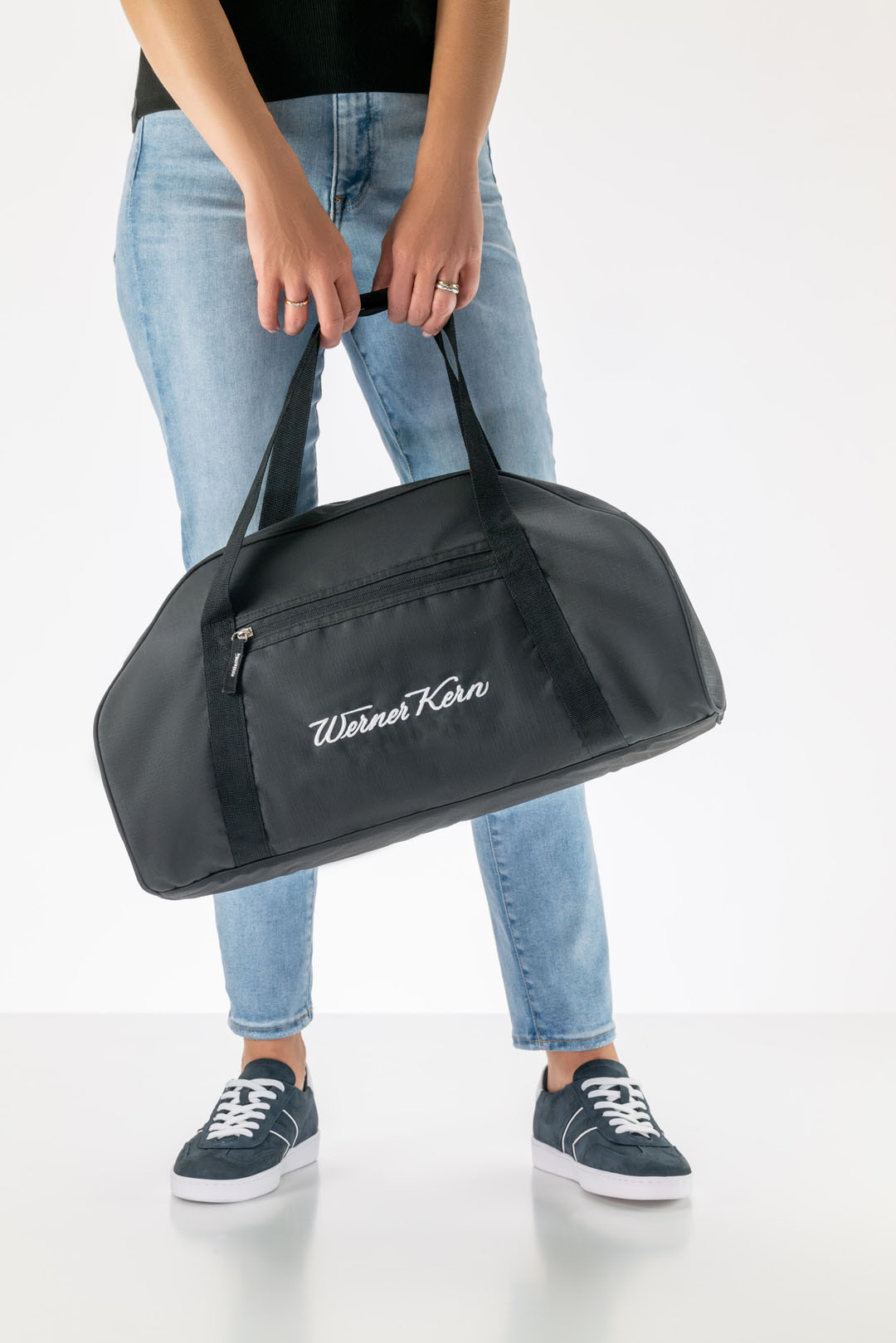 Sac de sport Werner Kern noir orné d'un logo blanc, porté par un mannequin en jean